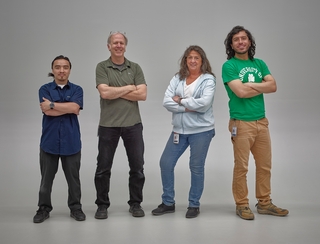 four people stand looking at the camera with their arms crossed.